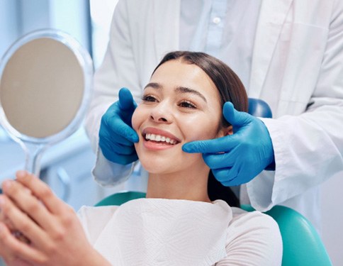 person smiling and looking in a mirror at the dental office