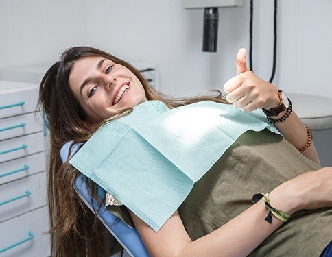 Woman in dental chair giving thumbs up after tooth extraction