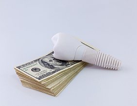 White dental implant leaning on stack of money