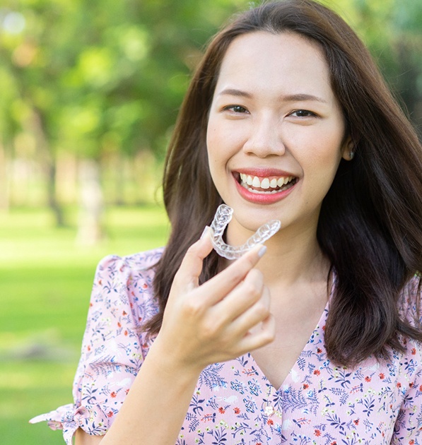 A young, female teenager wearing a floral blouse and preparing to insert a clear aligner that is part of her treatment with Invisalign in Tyler