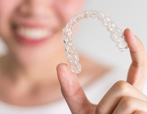 A person holding up a clear aligner between their thumb and forefinger