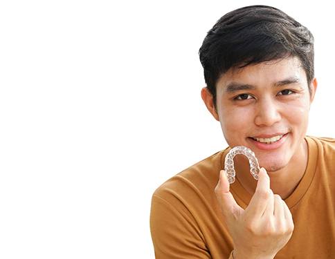 A young male teen wearing a tan shirt and holding his Invisalign aligner