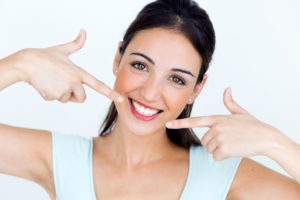 young woman pointing to her smile with veneers in Tyler 