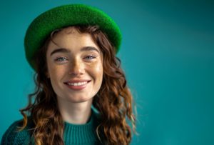 Woman with freckles in green hat smiling
